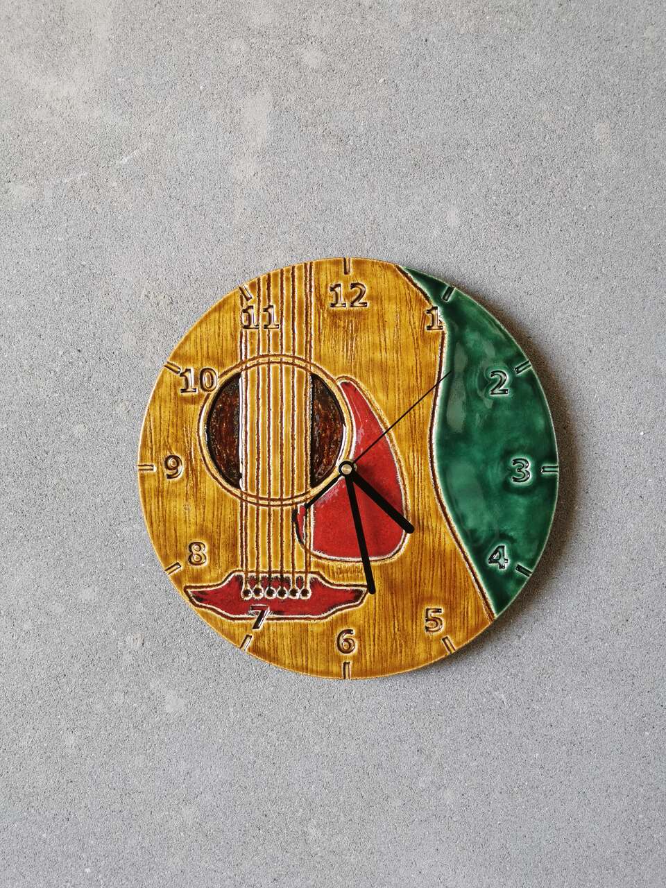 Ceramiczny zegar z motywem muzycznym na ścianie, przedstawia gitarę klasyzczną.