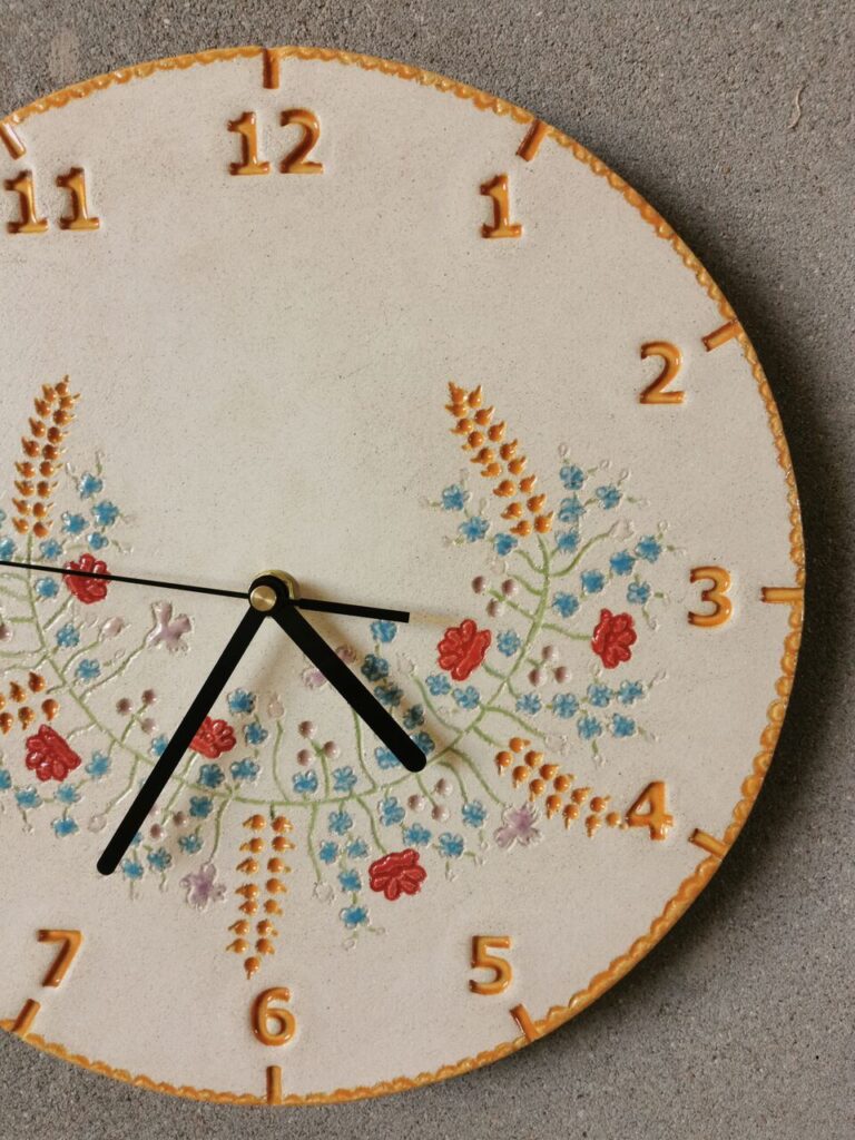 Zegar wianek zbóż i polnych kwiatów zawieszony na ścianie w ciepłych kolorach – idealny do wnętrz z dużą ilością zieleni.