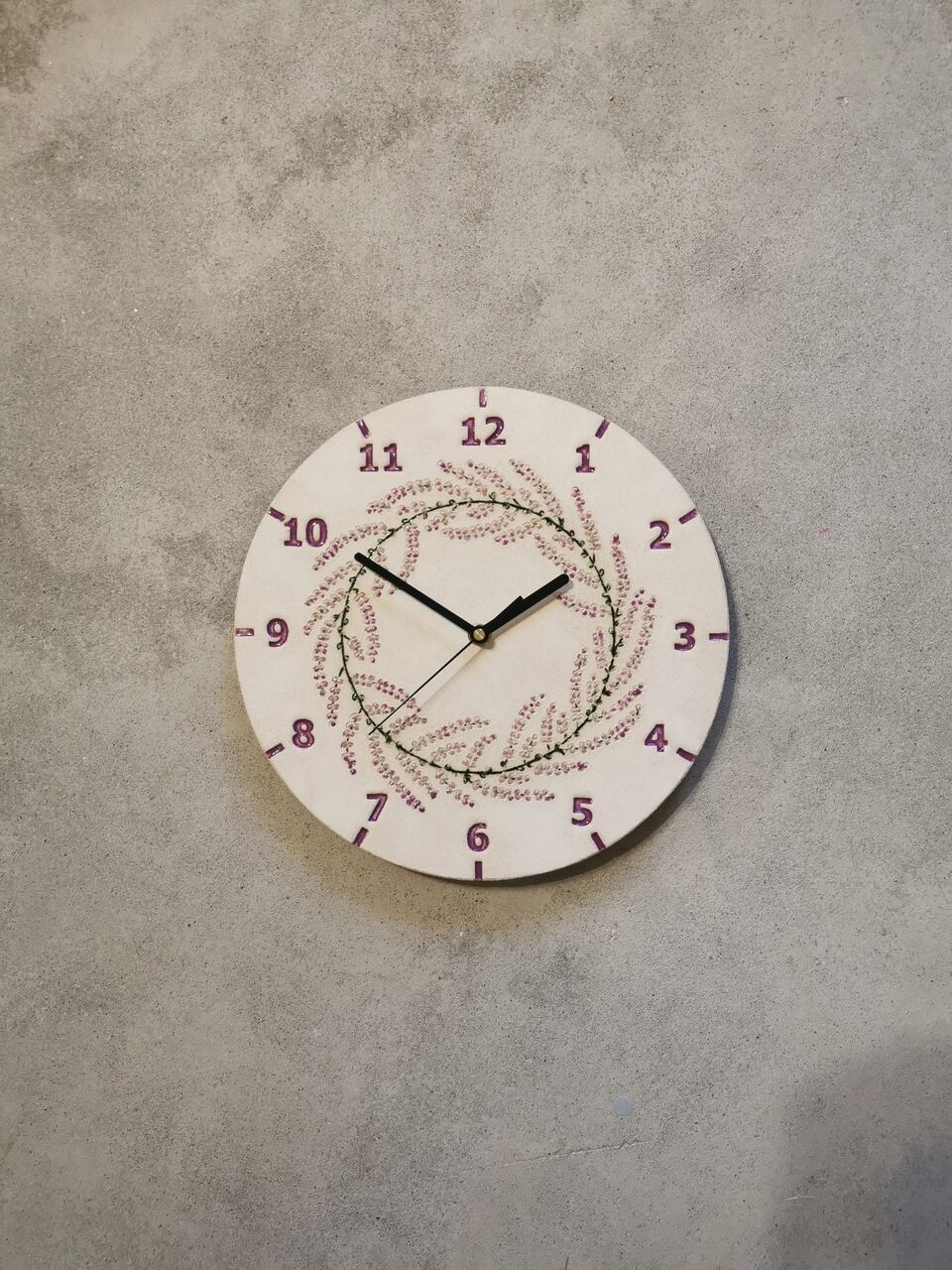 Ceramiczny zegar na szarej betonowej ścianie, przestawiający wianek z lawendy - Eweolo Ceramika