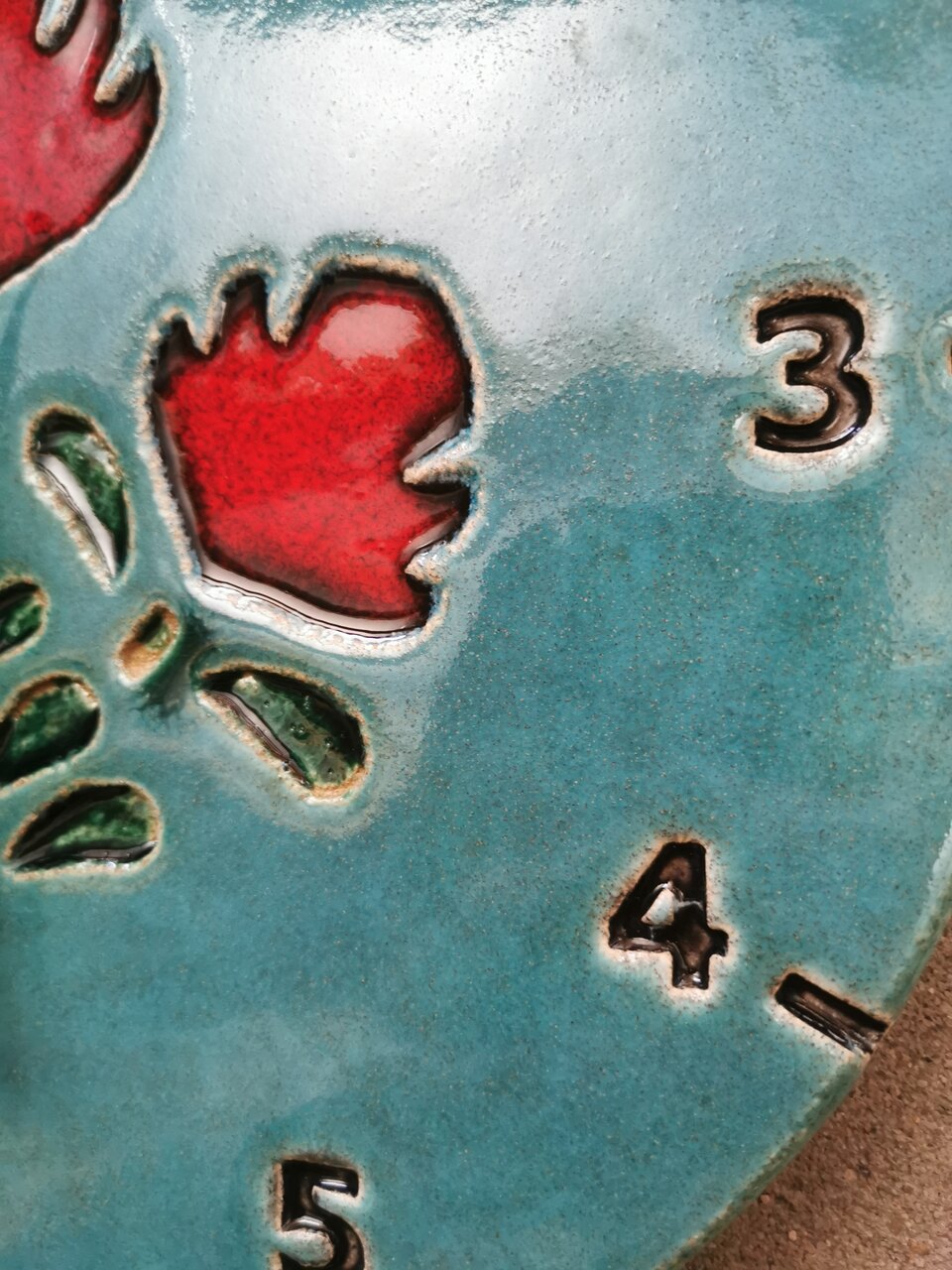 Detal ceramicznego zegara ściennego na zamówienie - soczyste niebieskie szkliwo i czerowony ludowy kwiat.