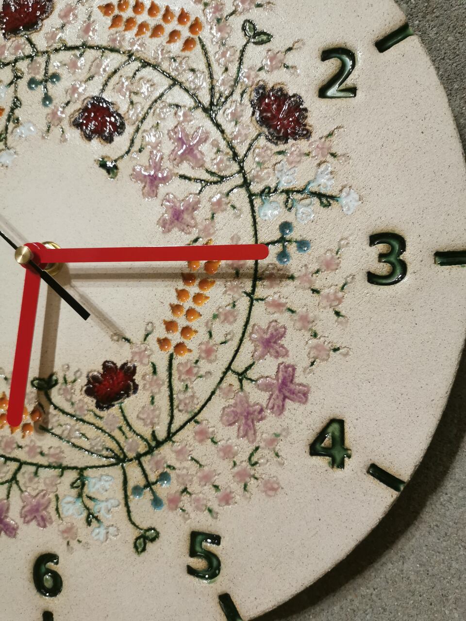 Zbliżenie na misterne, ręcznie lepione ceramiczne kwiaty na tarczy zegara kwietnego.