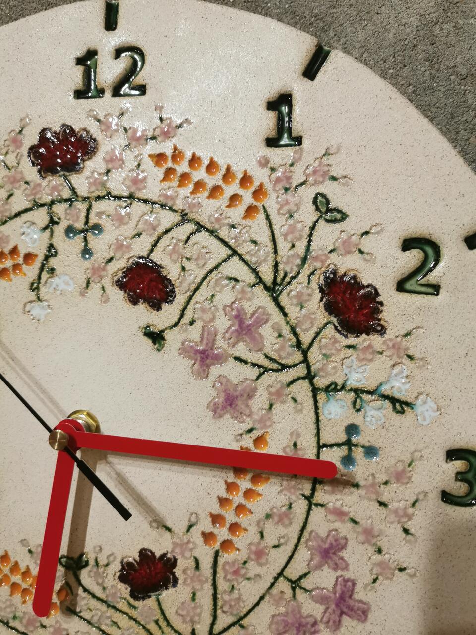 Zbliżenie na ceramiczny wianek na zegarze ściennym - kłosy zbóż, maki, chabry, niezapominajki.