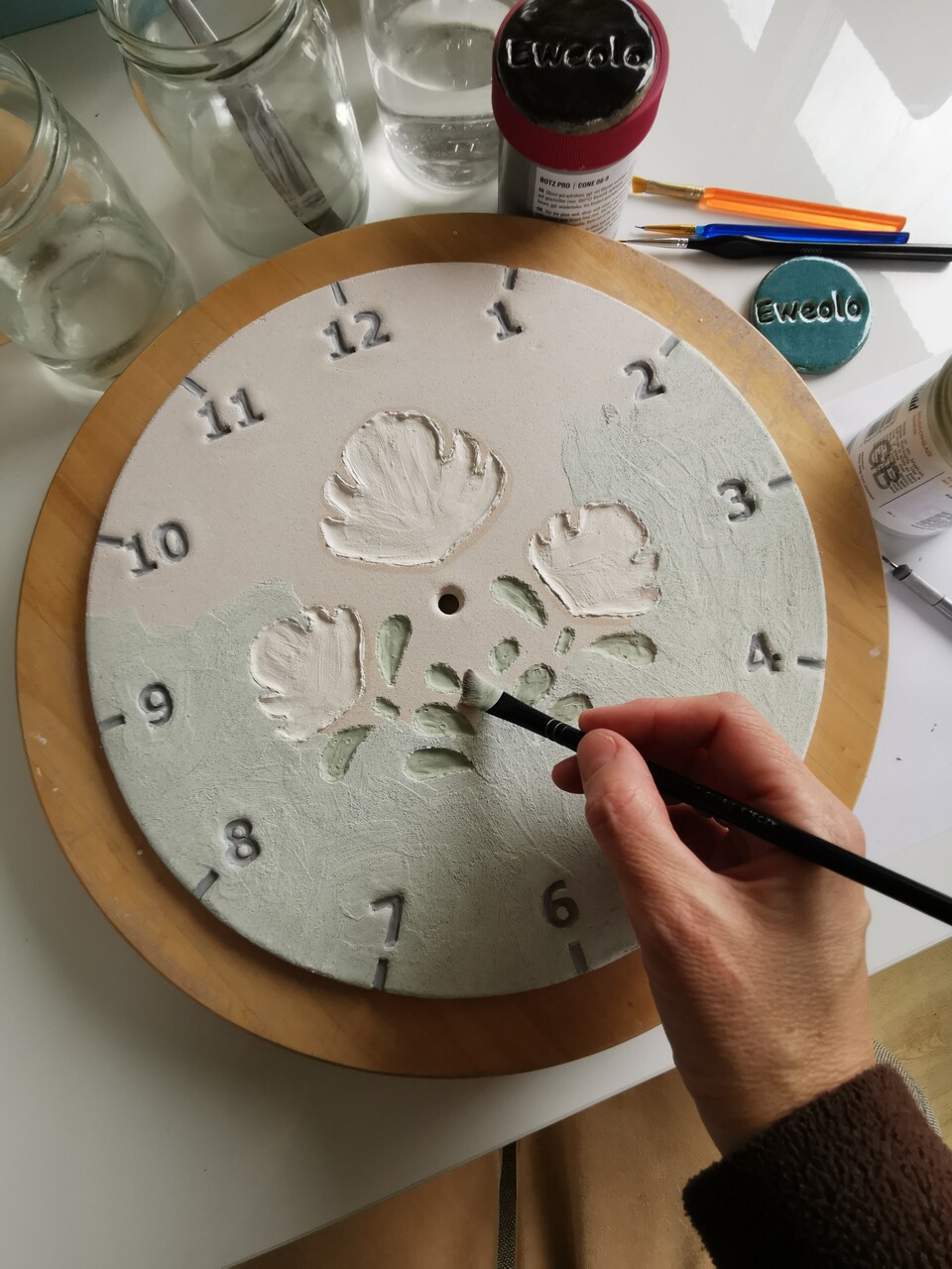 Ręczne malowanie niebieskim szkliwem kwiatów ludowych na tarczy ceramicznego zegara.