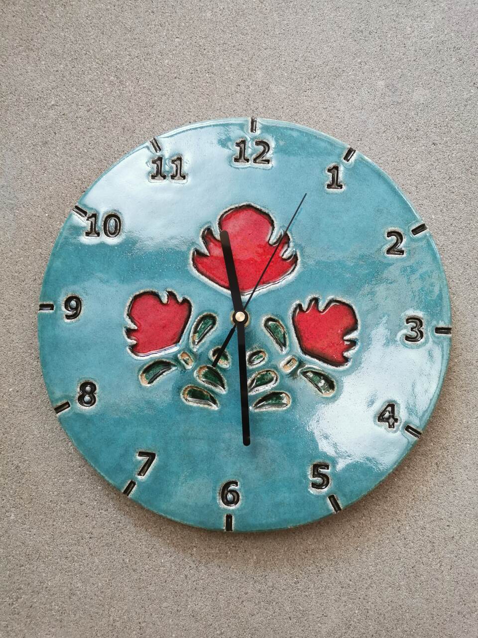 Zbliżenie na zegar ceramicznym przedstawiający czerowne ludowe kwiaty na soczyście niebieskim tle.