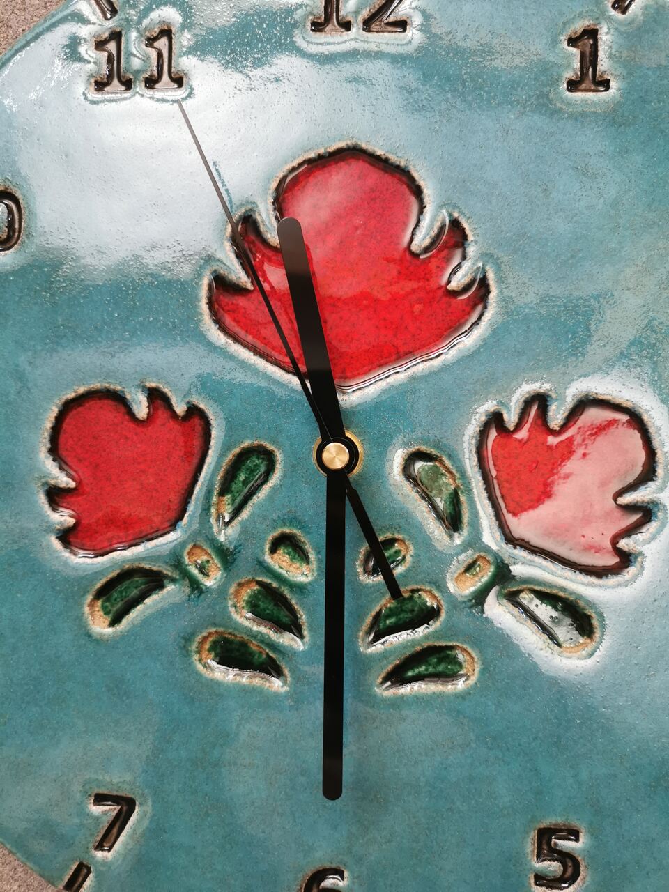 Zbliżenie na soczyście czerowone ludowe kwiaty na ceramicznym niebieskim zegarze ściennym.