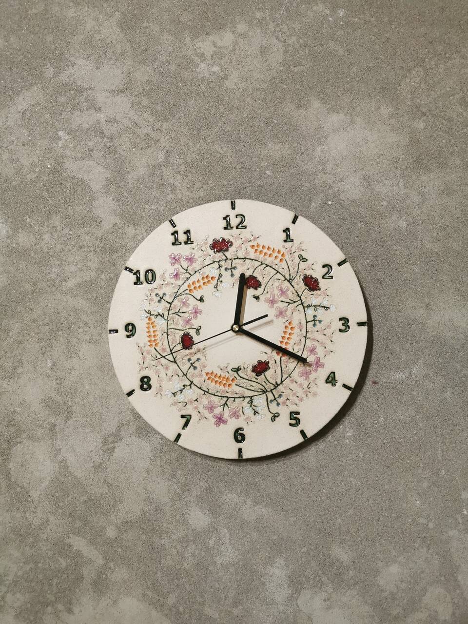 Wianek kwiatów na ceramicznym zegarze ściennym widok na betonowej ścianie.