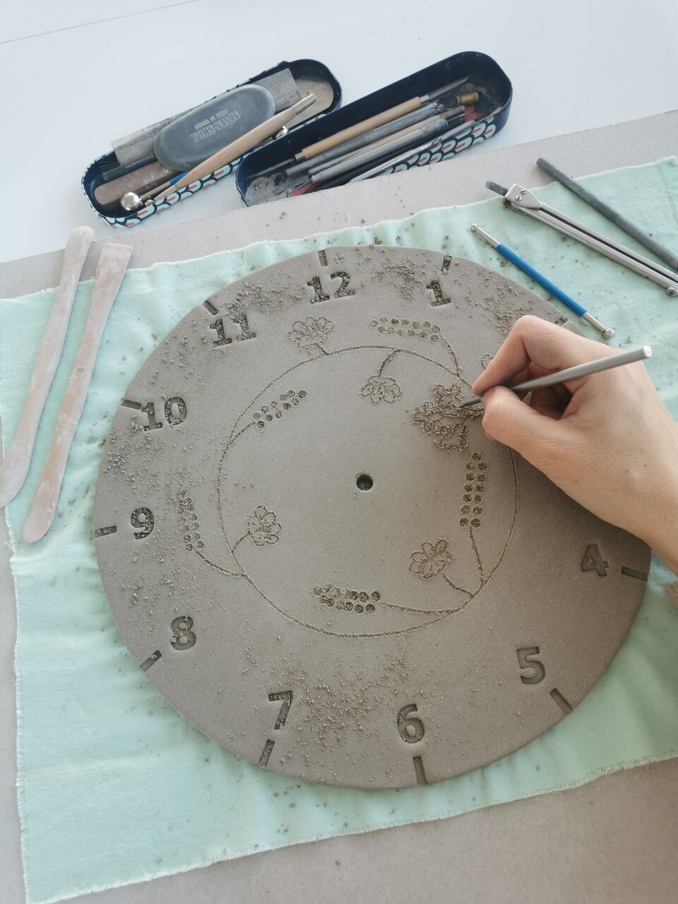 Rękodzielnik dłubie wzór na ceramicznej tarczy zegara.
