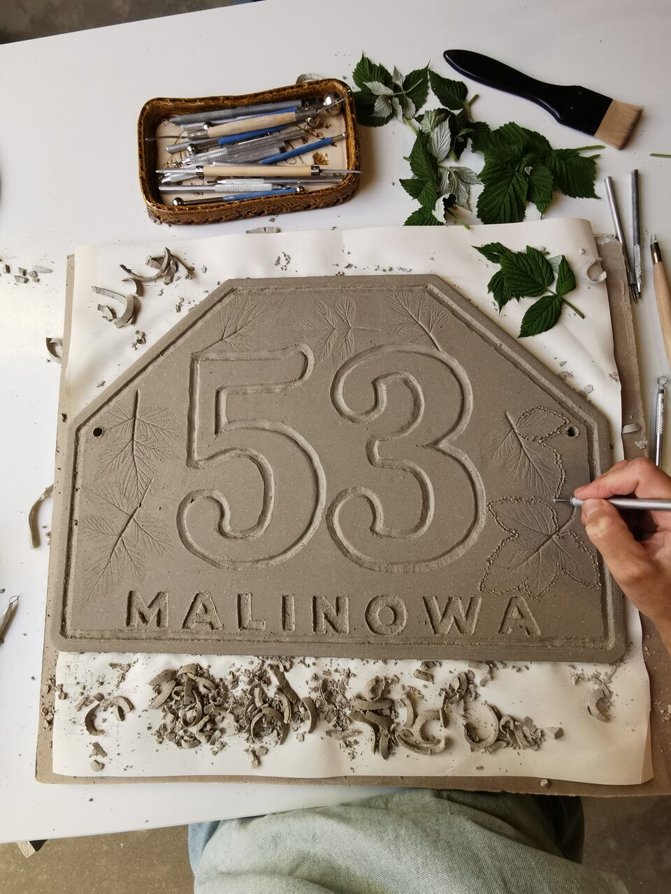 Artysystyczny szyld adresowy z gliny w trakcie ręcznego formowania numeru domu.