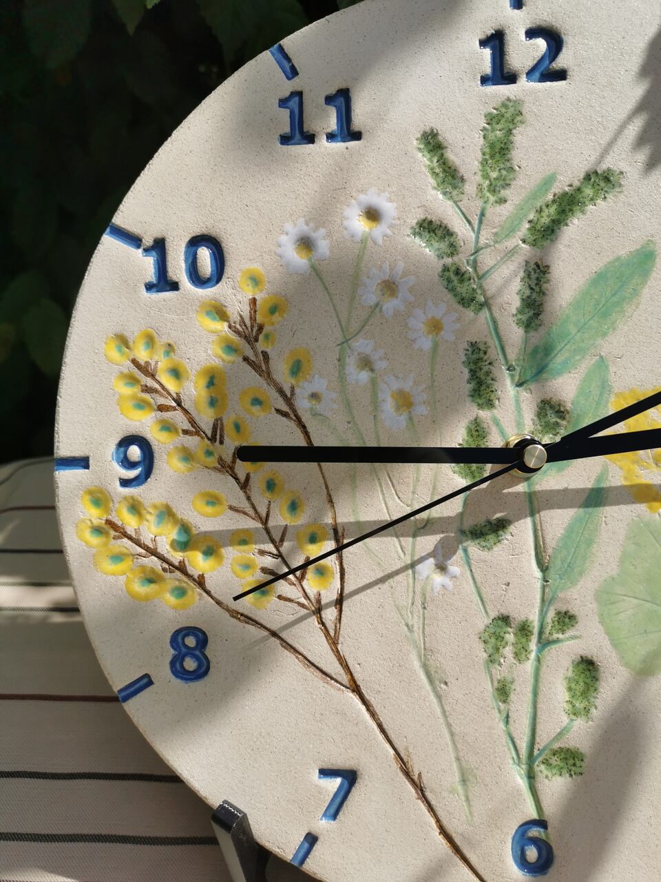 Zbliżenie na żółto zieloną tarczę zegara ceramicznego na ścianę z roslinami.