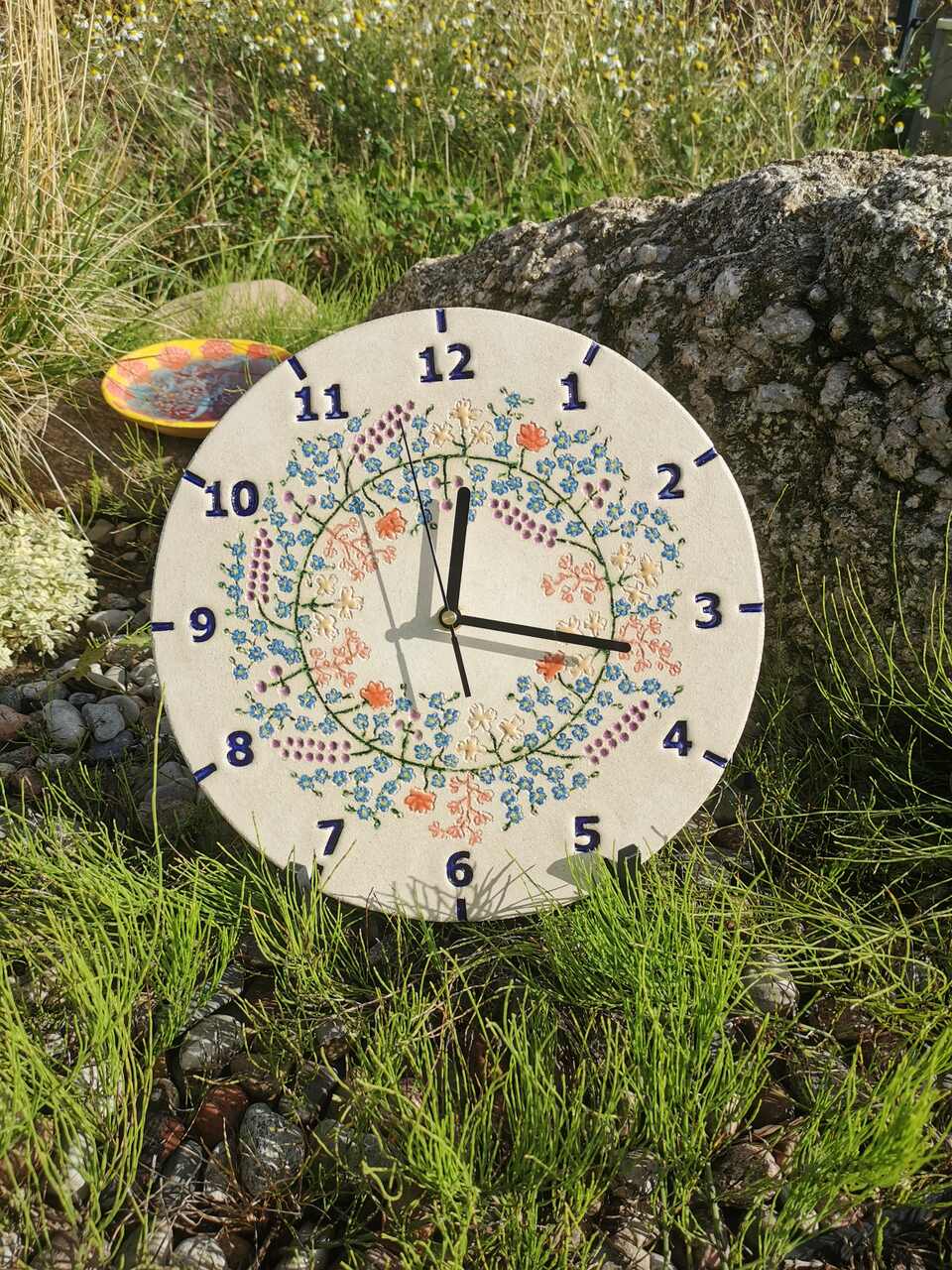 Ceramiczny zegar na ściane niebieskie kwiaty w wianku.