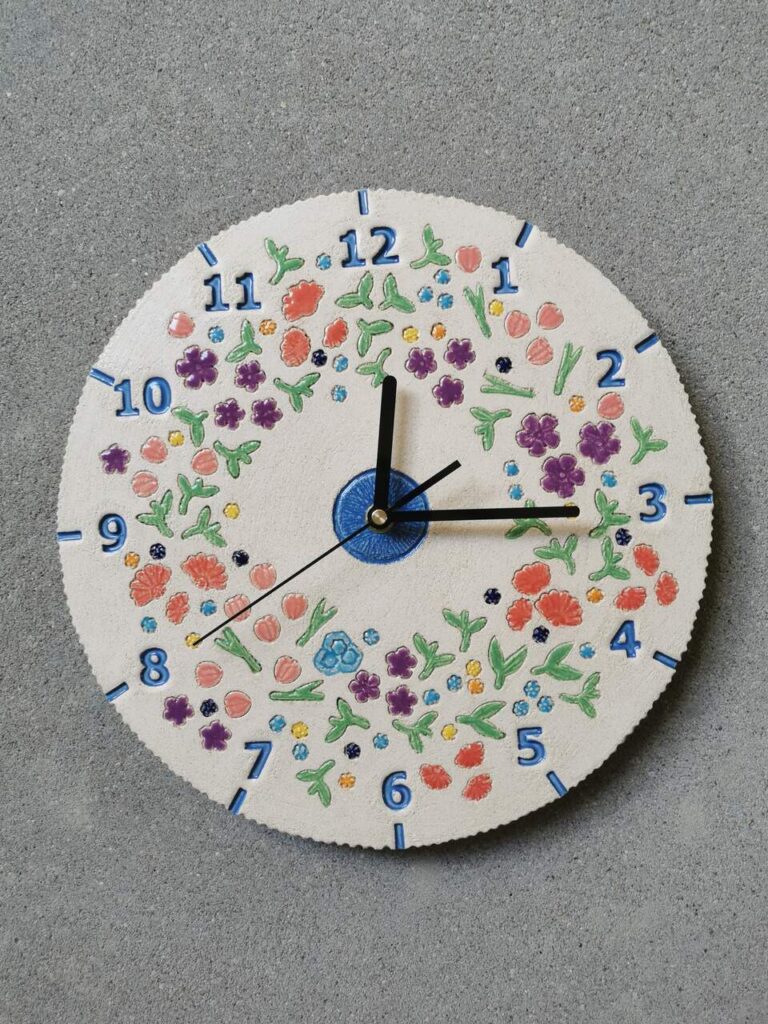 Ceramiczny zegar ścienny na zamówienie przedstawiający łąkę kwietną na tle naturalnej glinianej tarczy.