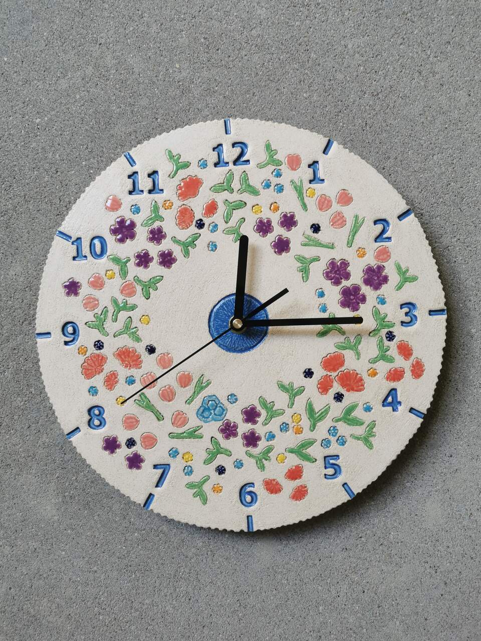 Ceramiczny zegar ścienny na zamówienie przedstawiający łąkę kwietną na tle naturalnej glinianej tarczy.