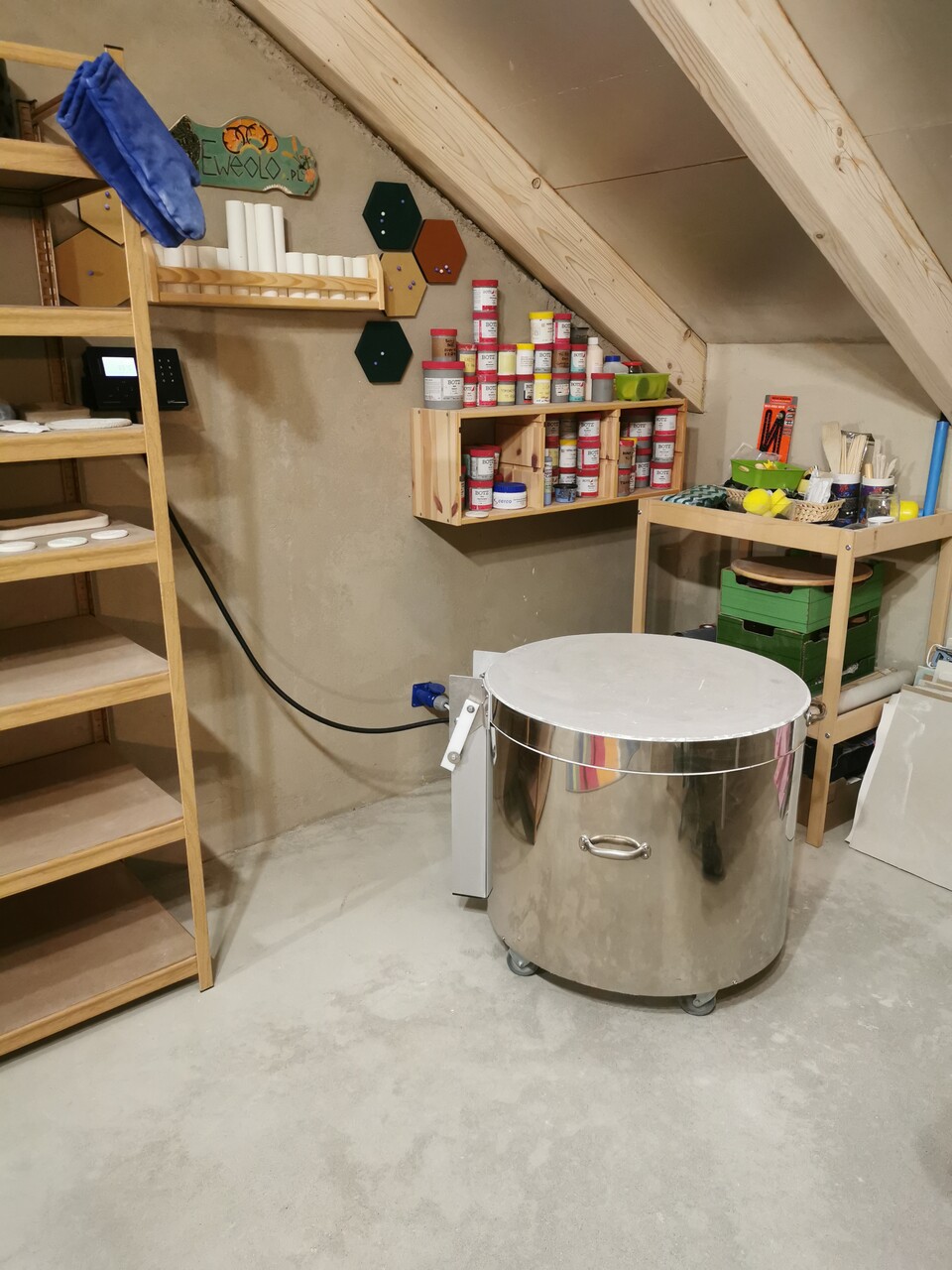 Pracownia ceramiczna eweolo, wnętrze z półkami, piecem do wypału i szkliwami w tle.